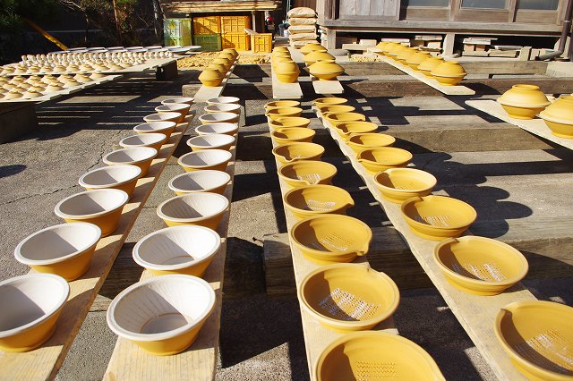 This is an Onta Ware workshop in the village of Onta, Oita, Japan. In the front yard of the workshop, a lot of formed bowls are drying in the sun on wooden boards.