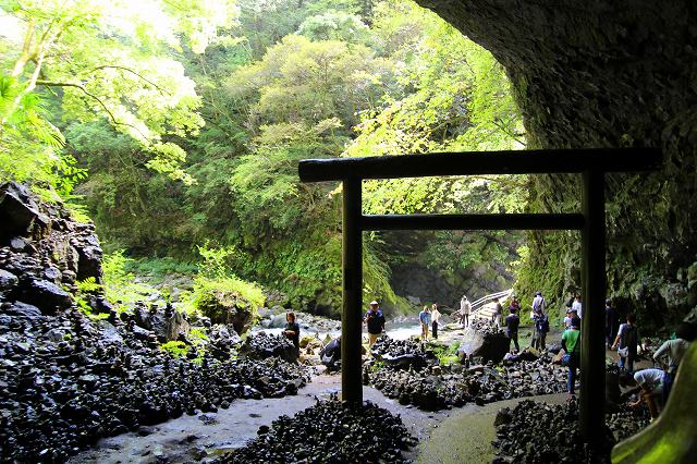 This is Amanoyasugawara riverbank in Takachiho, Miyazaki, Japan. There is a large cave with a torii gate and many piled up stones.