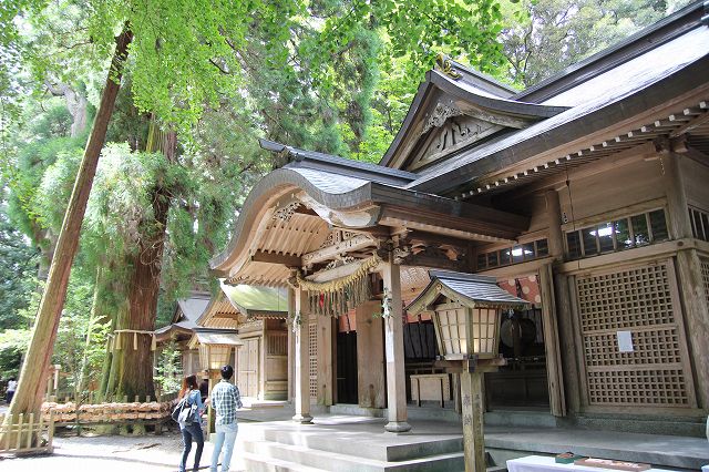 This is the divine wooden Takachiho Shrine in MIyazaki, Japan. Two worshippers are standing in front of the Takachiho Shrine.