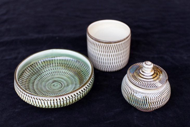 This is a photo of Kogata pottery made using traditional methods. There are three pieces in a row: a small plate, a teacup, and a small jar with a lid.